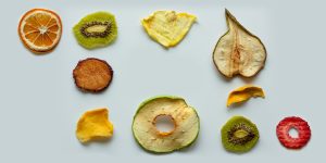 sobr eun fondo verde claro podemos ver diferentes frutas (una naranja, un Kiwi, un platano, una frutilla) deshidratadas