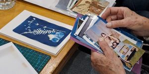 Imagen del taller de bitácoras del exilio en la que dos manos visualizan fotos antiguas sobre una mesa en la que encontramos una cianotipia